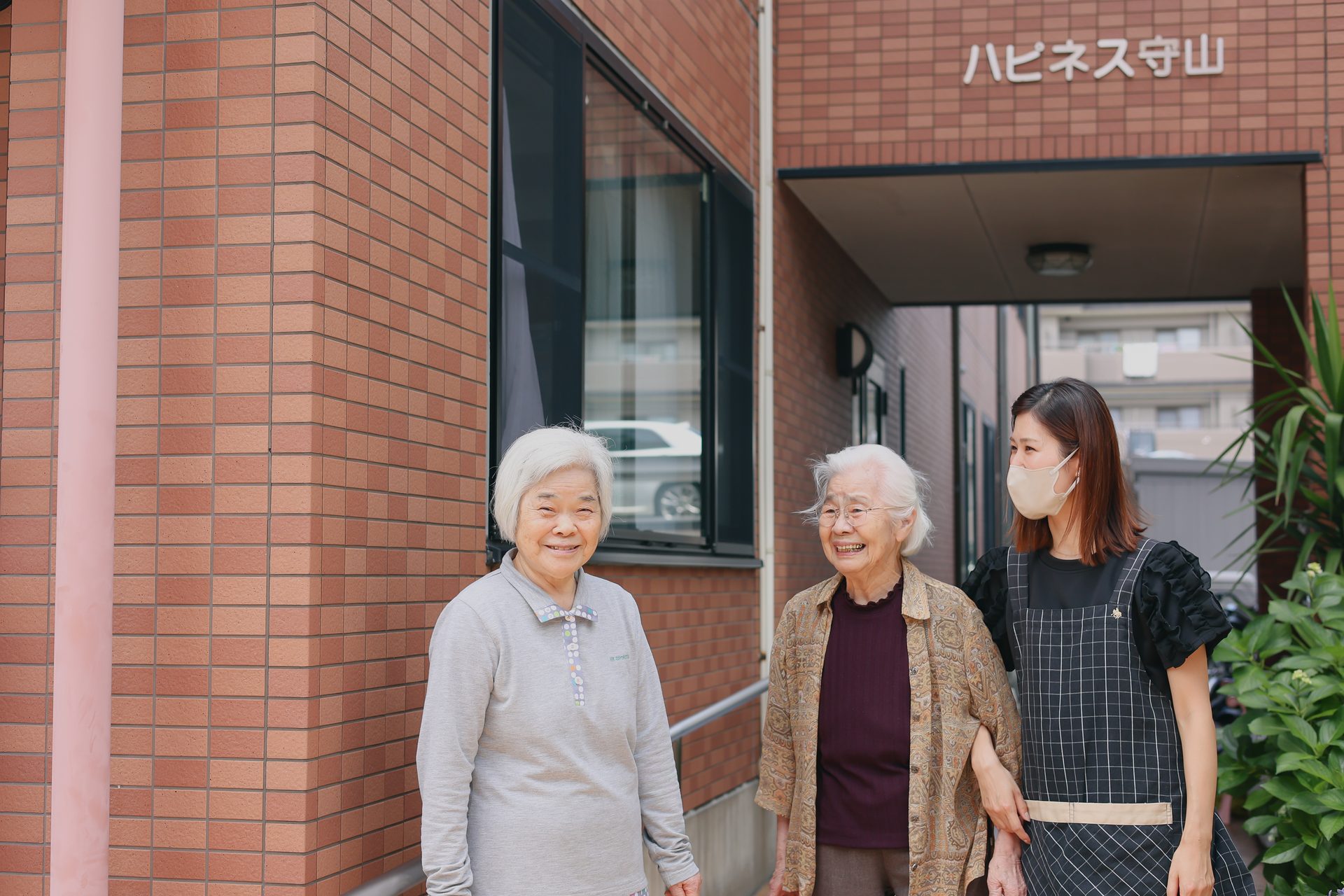 ハピネス守山の玄関前で微笑む入居者様とスタッフ